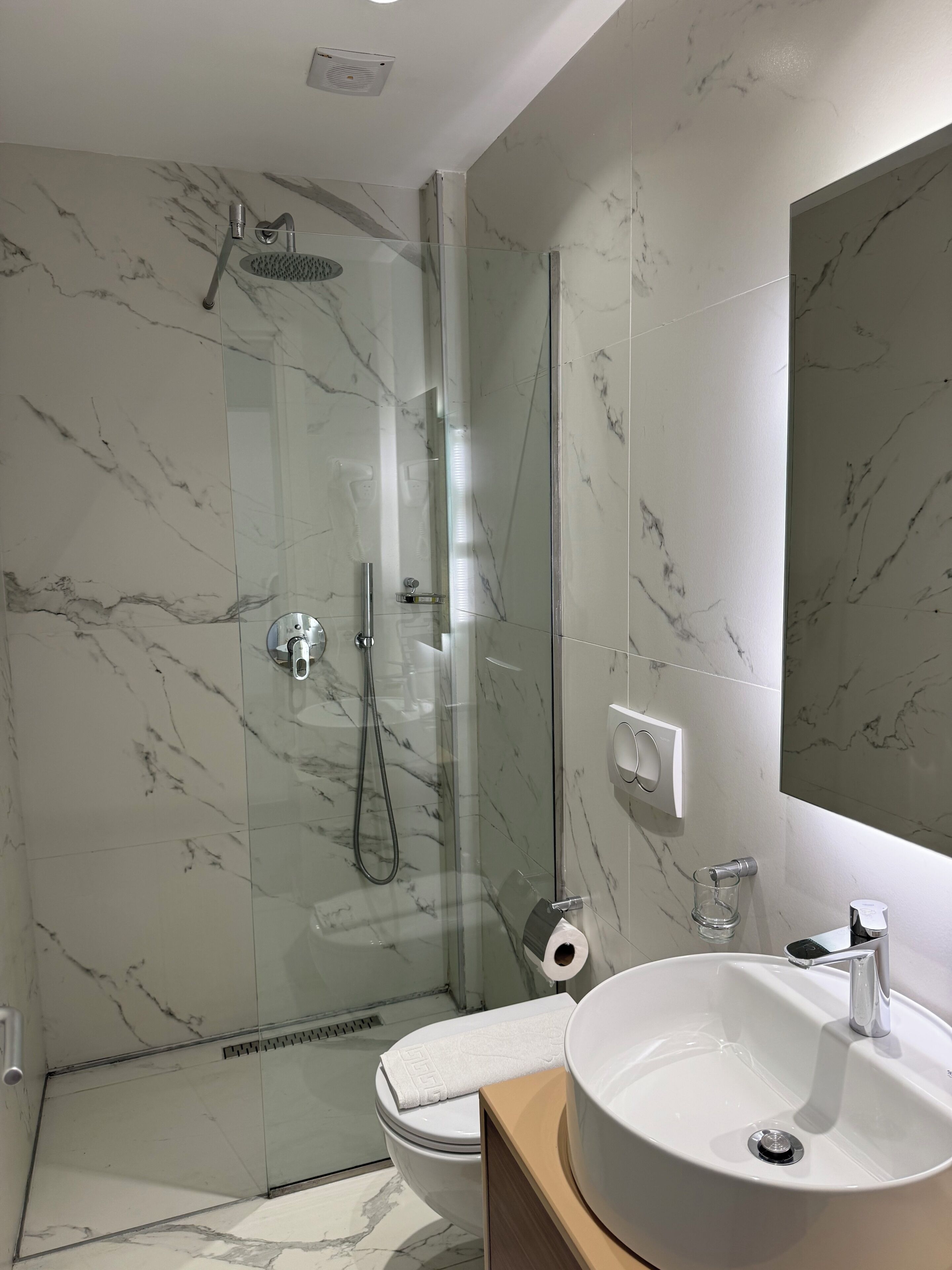 Un baño moderno con ducha acristalada, lavabo blanco y un espejo grande.