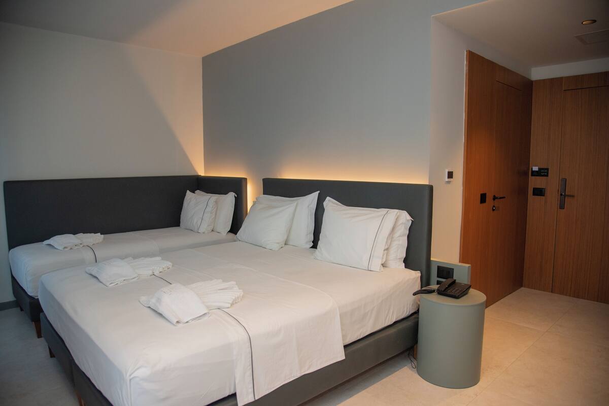 Ett modernt hotellrum med två sängar, ett nattduksbord med en telefon och en dörr av trä.