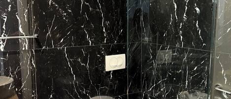 Ein modernes Badezimmer mit schwarzen Marmorwänden, einer Duschkabine aus Glas und zwei Waschbecken.