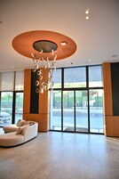 Un lobby amplio con una lámpara araña moderna, ventanas grandes y una zona de estar.