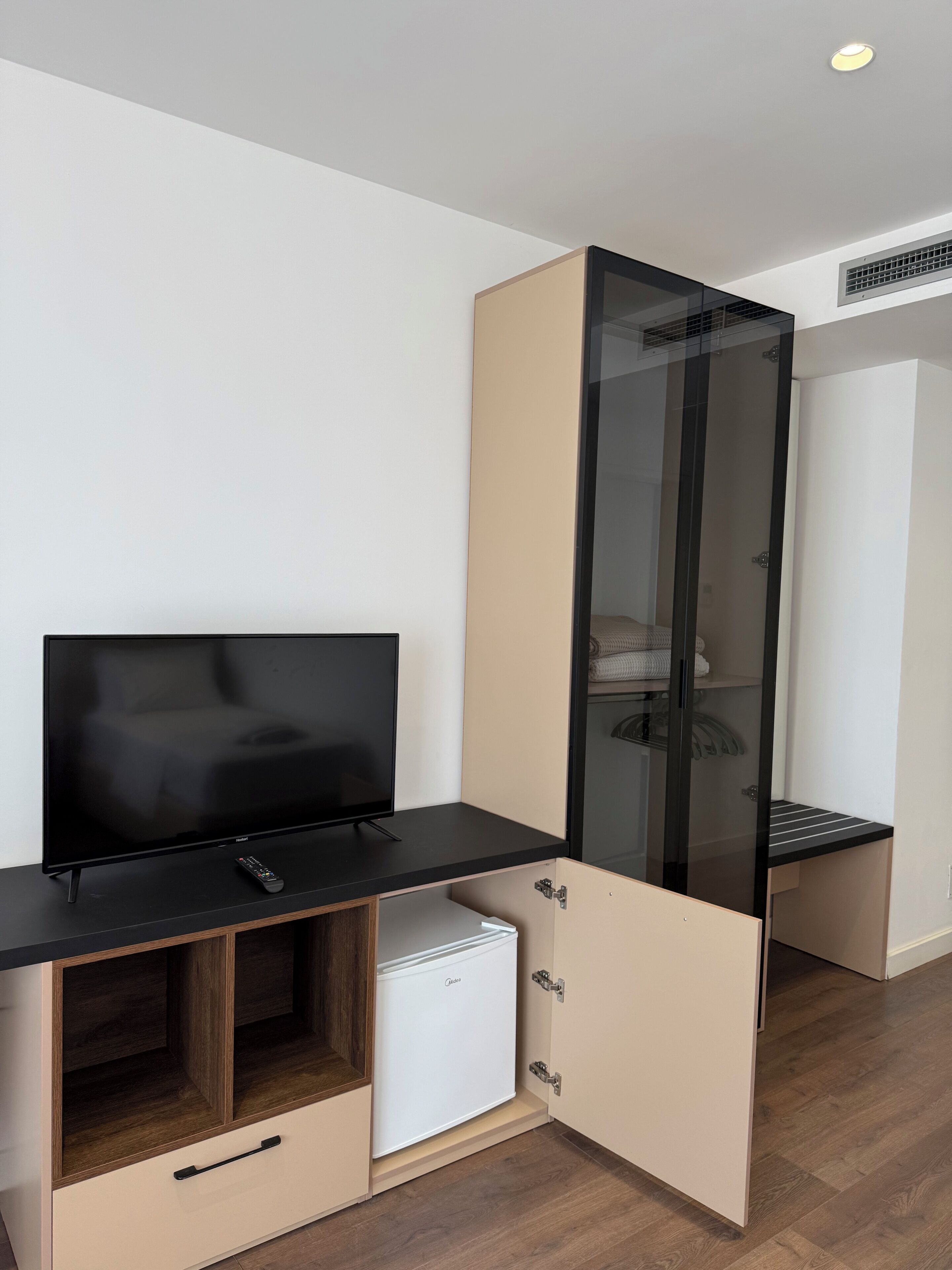 A corner room with a television, a small refrigerator, and a wardrobe with a sliding door.