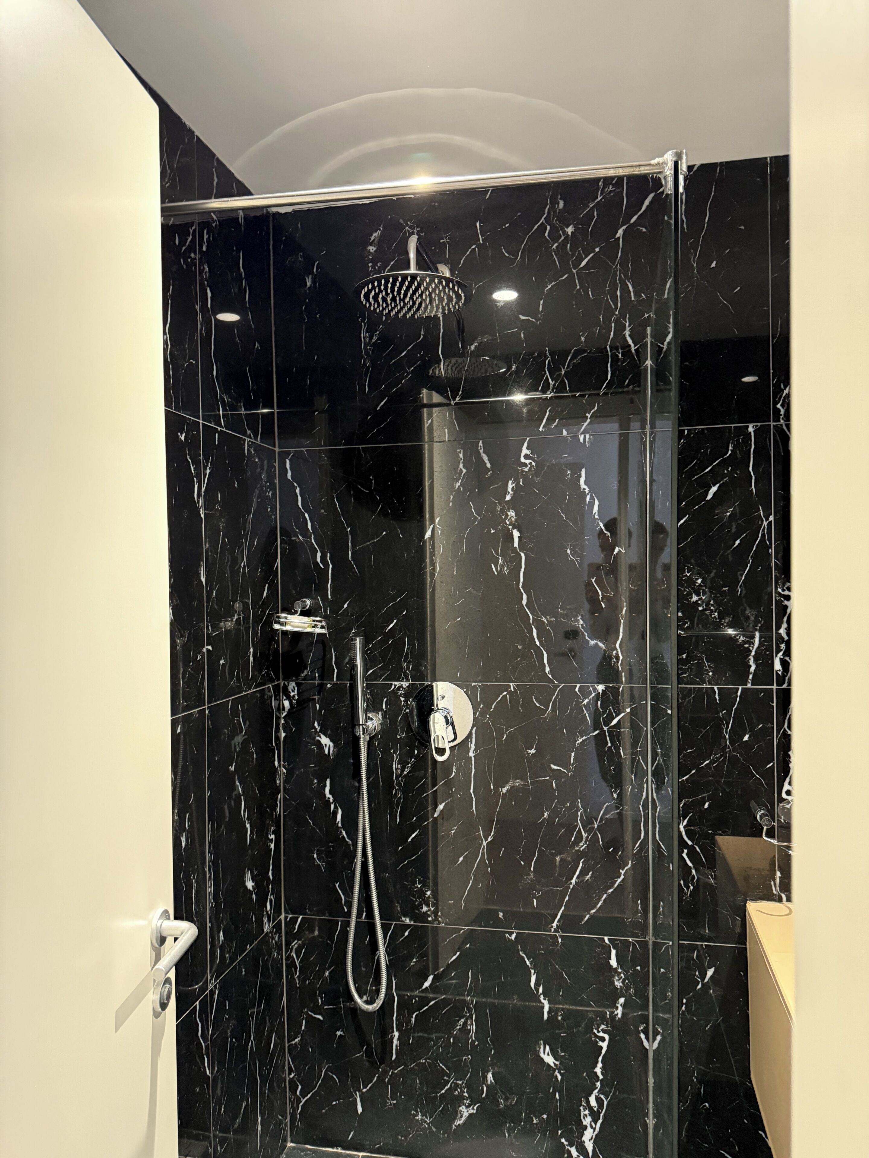 A modern bathroom with black marble tiles, a glass-enclosed shower, and a visible showerhead.