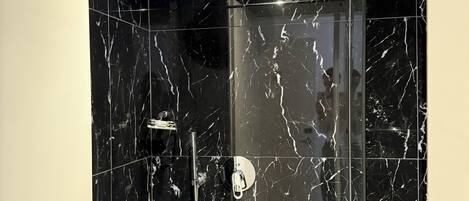 A modern bathroom with black marble tiles, a glass-enclosed shower, and a visible showerhead.