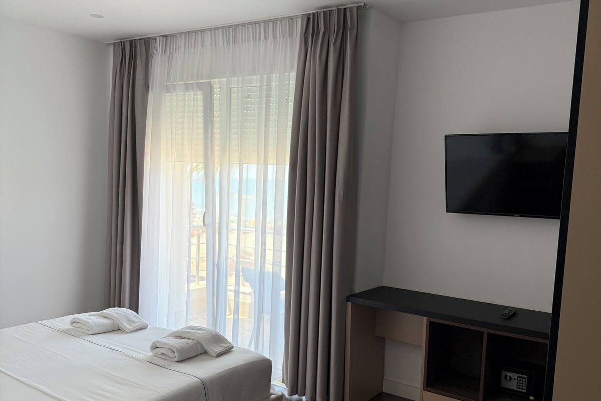Ett hotellrum med en säng, ett skrivbord, en tv och ett fönster med gardiner.