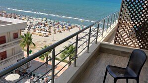 A balcony with a view of a beach, a pool, and a building with a sign. - Adria Palace Hotel (Rrashbull)