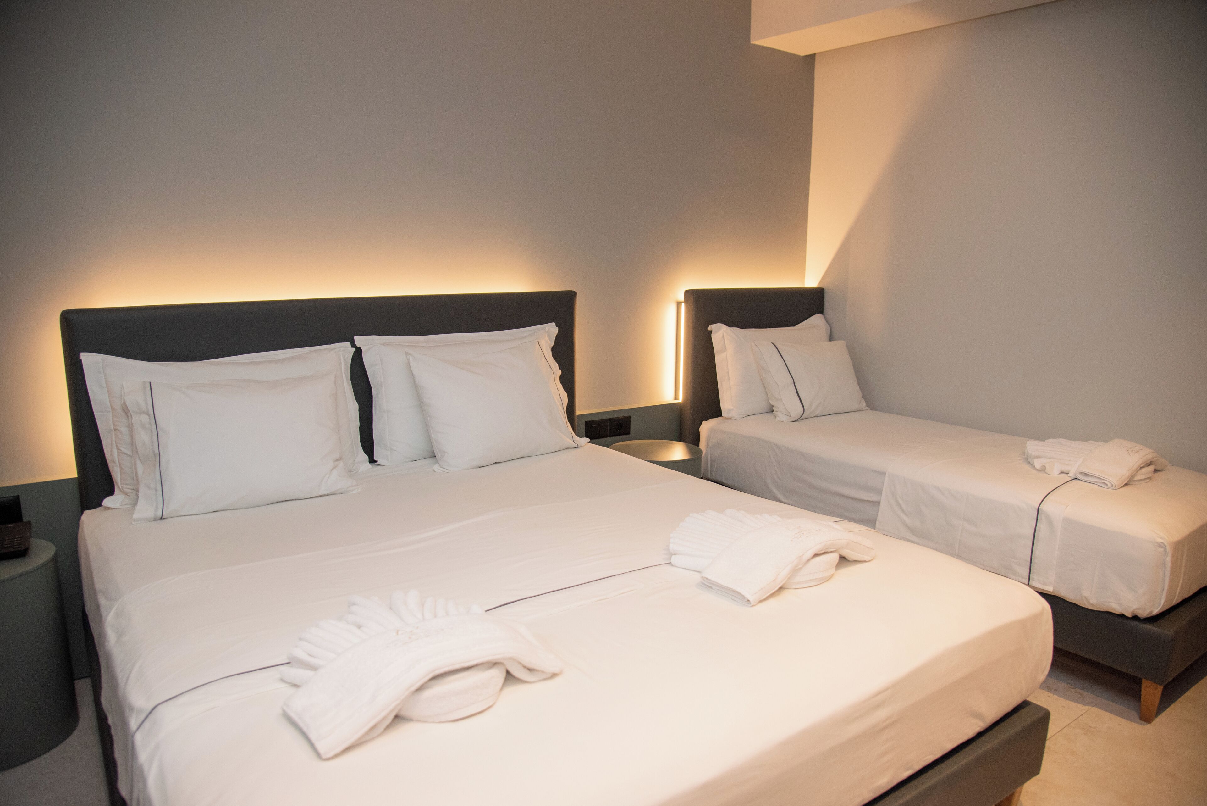 Une chambre d’hôtel avec deux lits, chacun agrémenté de draps et d’oreillers blancs, une table de chevet avec une lampe, et une serviette soigneusement pliée posée sur le plus grand des lits.