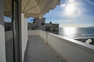 Un balcón con vista al mar, un edificio blanco y un cielo despejado.