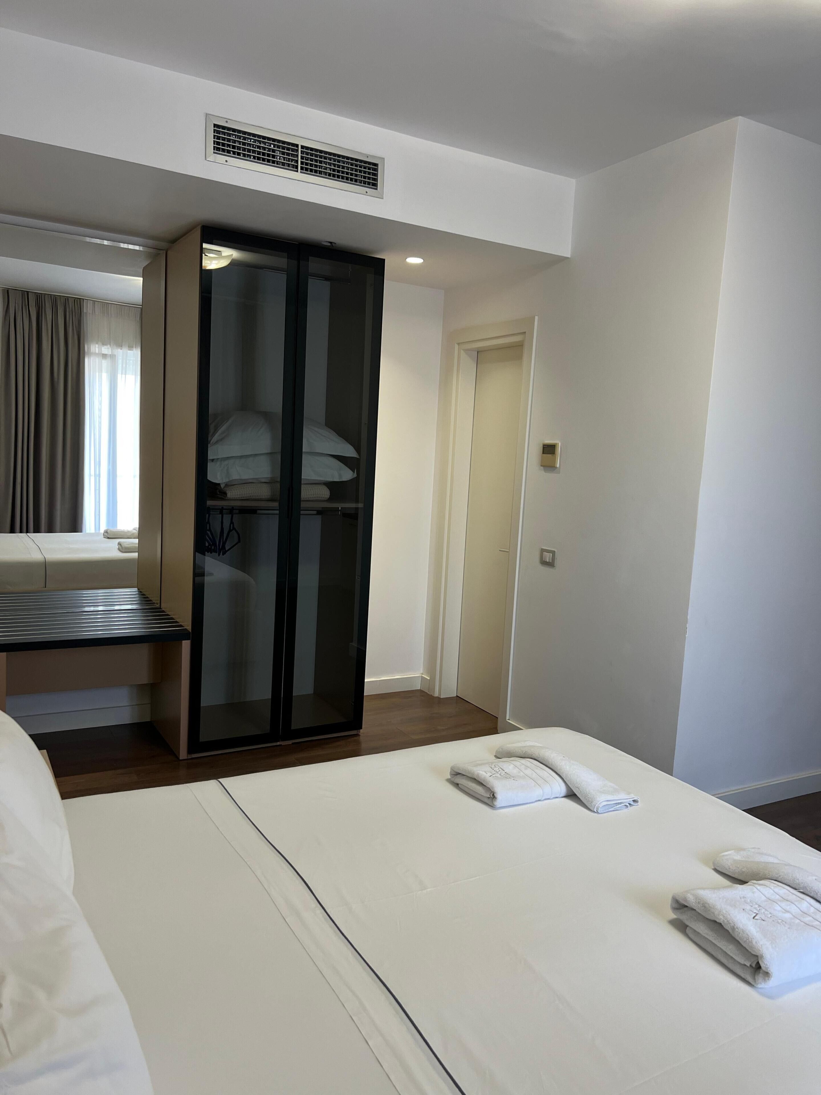 Una habitación de hotel con cama, armario, escritorio y ventana con cortinas.