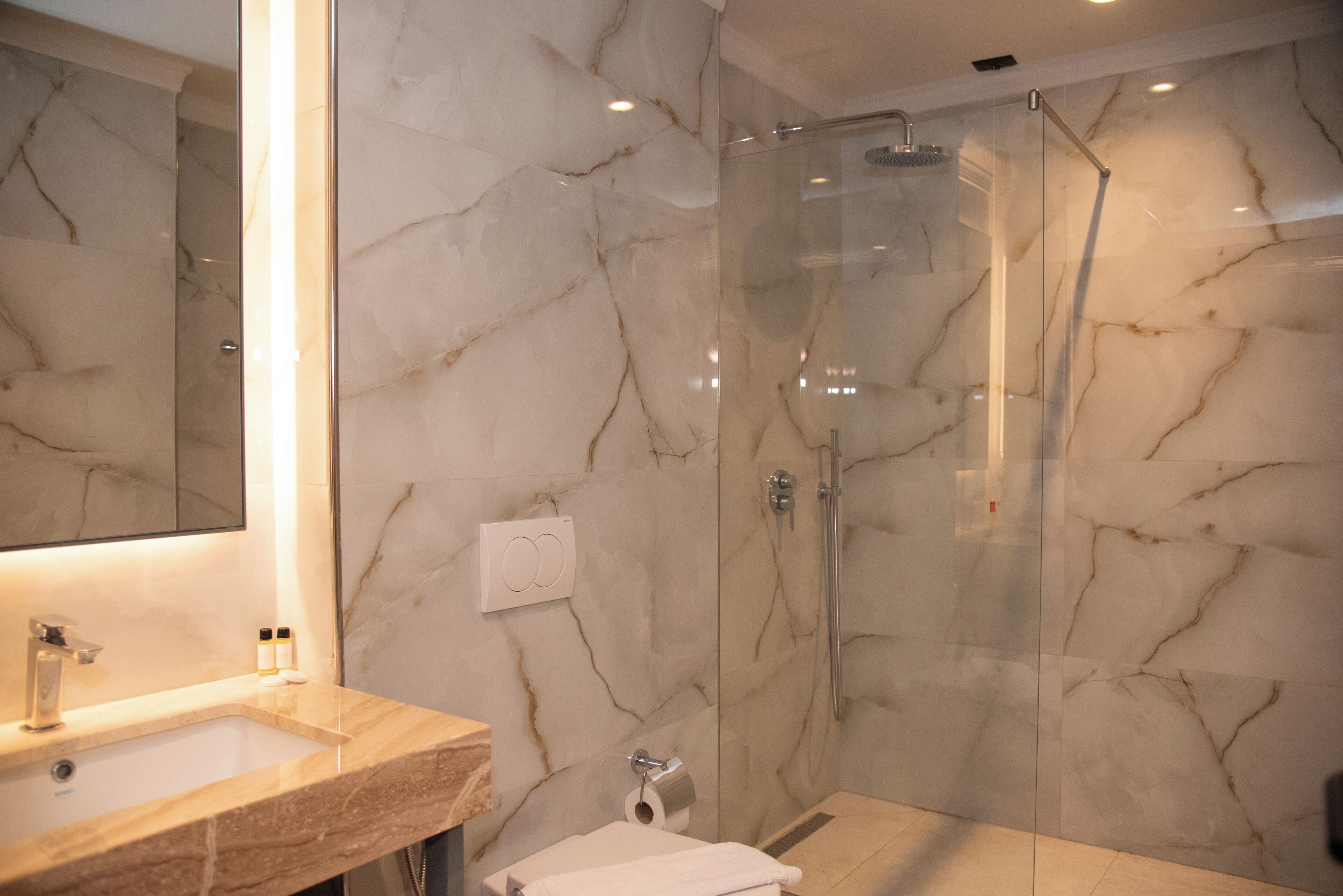 A modern bathroom with a marble vanity, a glass-enclosed shower, and a large mirror.
