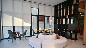 A modern interior with a white sectional sofa, a round table with chairs, and a black shelving unit. - Adria Palace Hotel (Rrashbull)