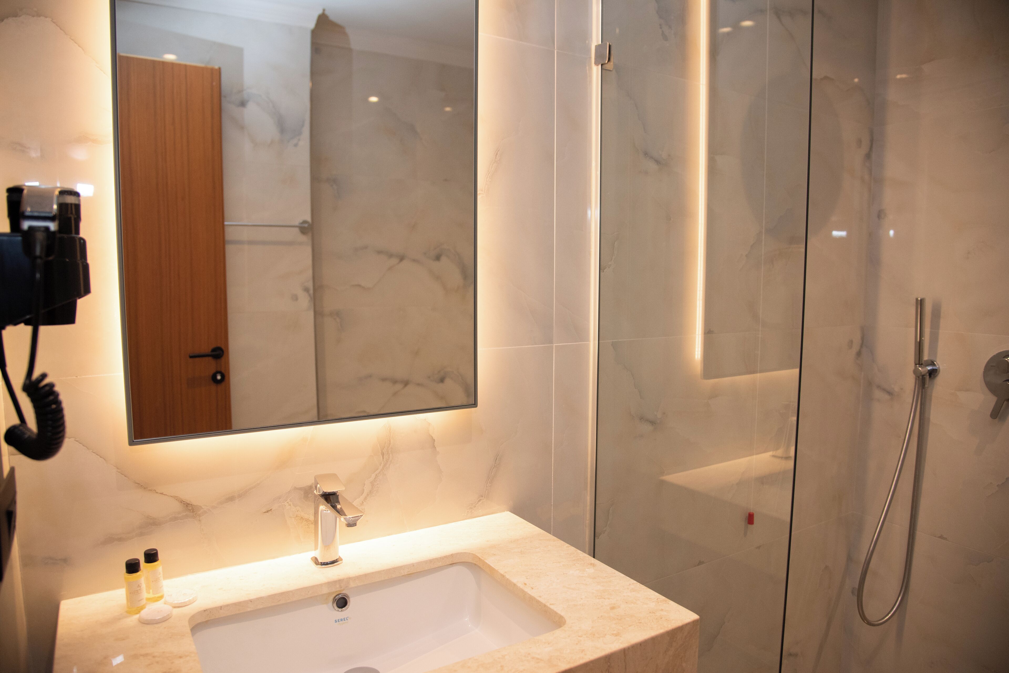 A modern bathroom with a marble sink, a large mirror, and a glass-enclosed shower.