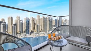Un balcón con vista a la ciudad, dos sillas de mimbre, una mesita con croissants y bebidas, y un vaso de jugo de naranja.