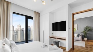 Una habitación de hotel moderna con una cama grande, un televisor montado en la pared, un escritorio pequeño y vistas a la ciudad.