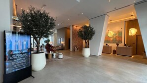 Un moderno vestíbulo de hotel con grandes macetas, un mostrador de recepción y una pared con diseño ornamental.