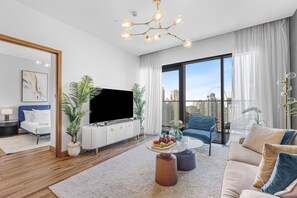 Ein modernes Wohnzimmer mit Flachbildfernseher, einer Couch, einem Couchtisch mit Obst und einem großen Fenster mit Blick auf die Stadt.