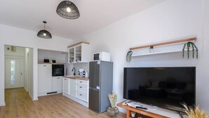 A modern kitchen with white cabinets, a built-in oven, and a large refrigerator. There is a wooden dining table with a TV and a shelf below it. - Comfortable 2-Bedroom Family Apartment in the small, quiet street. (Orebic)