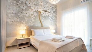 A modern bedroom with a large bed, a nightstand with a lamp, a wall mural, and a chandelier. - Casa Gardenia -modern apartment next to the beach and near old town (Chania)
