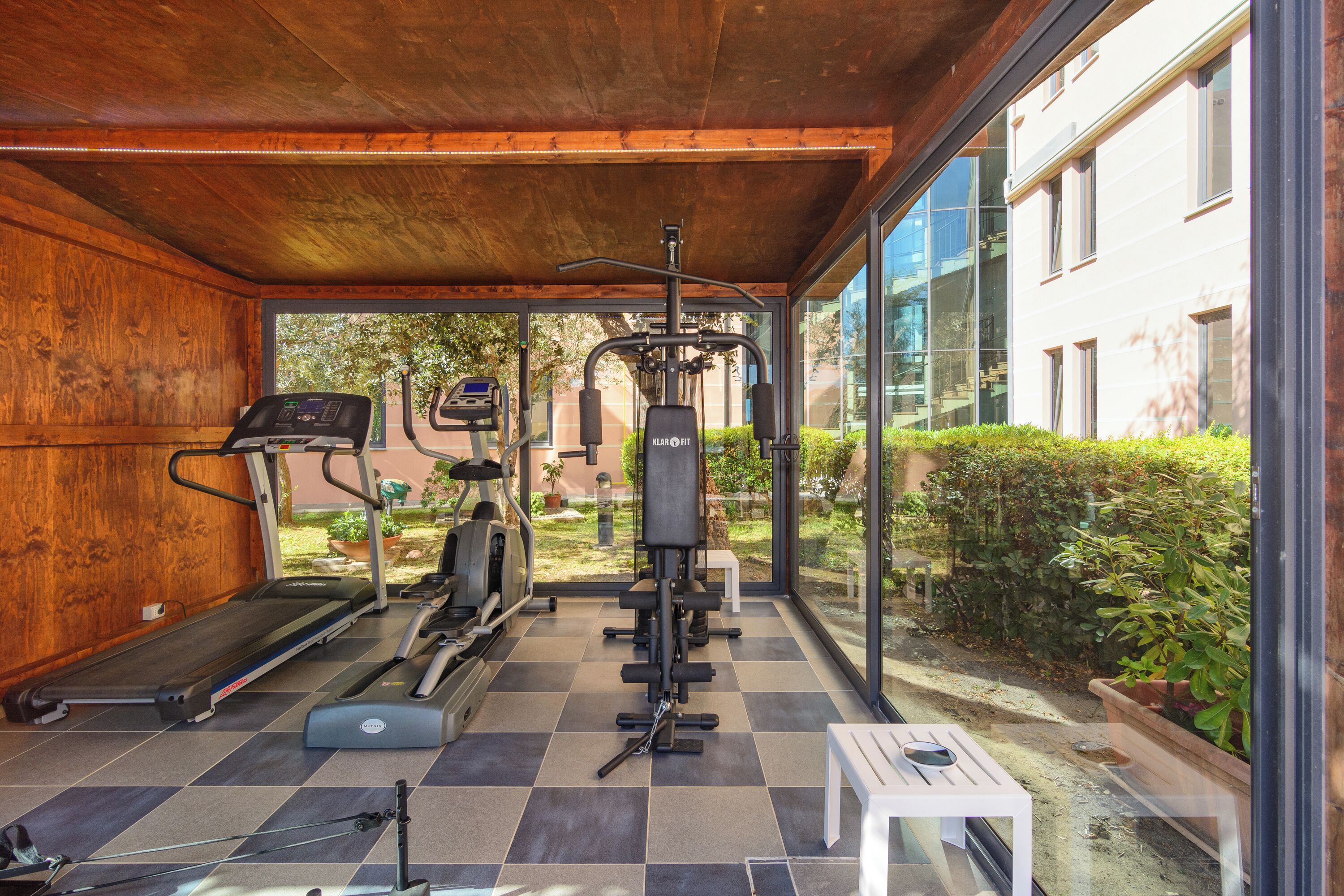 A covered gym area with exercise equipment, a treadmill, and a bench.
