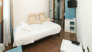 Una camera d'albergo con un letto, una scrivania, una TV a parete e un'apertura che conduce a un'altra stanza.