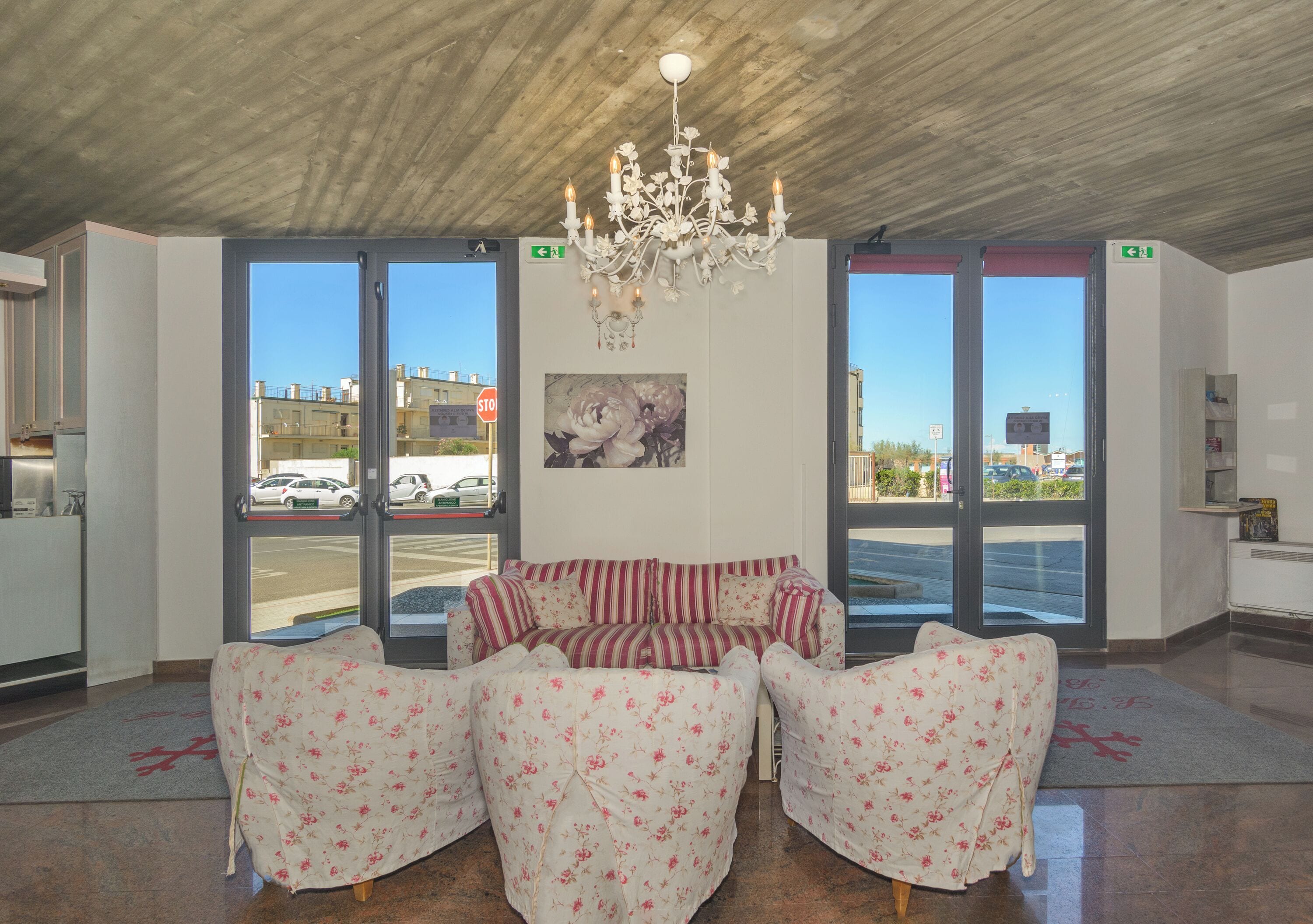 Un vestíbulo con candelabro, un conjunto de sofás y ventanas amplias con vista a la calle.
