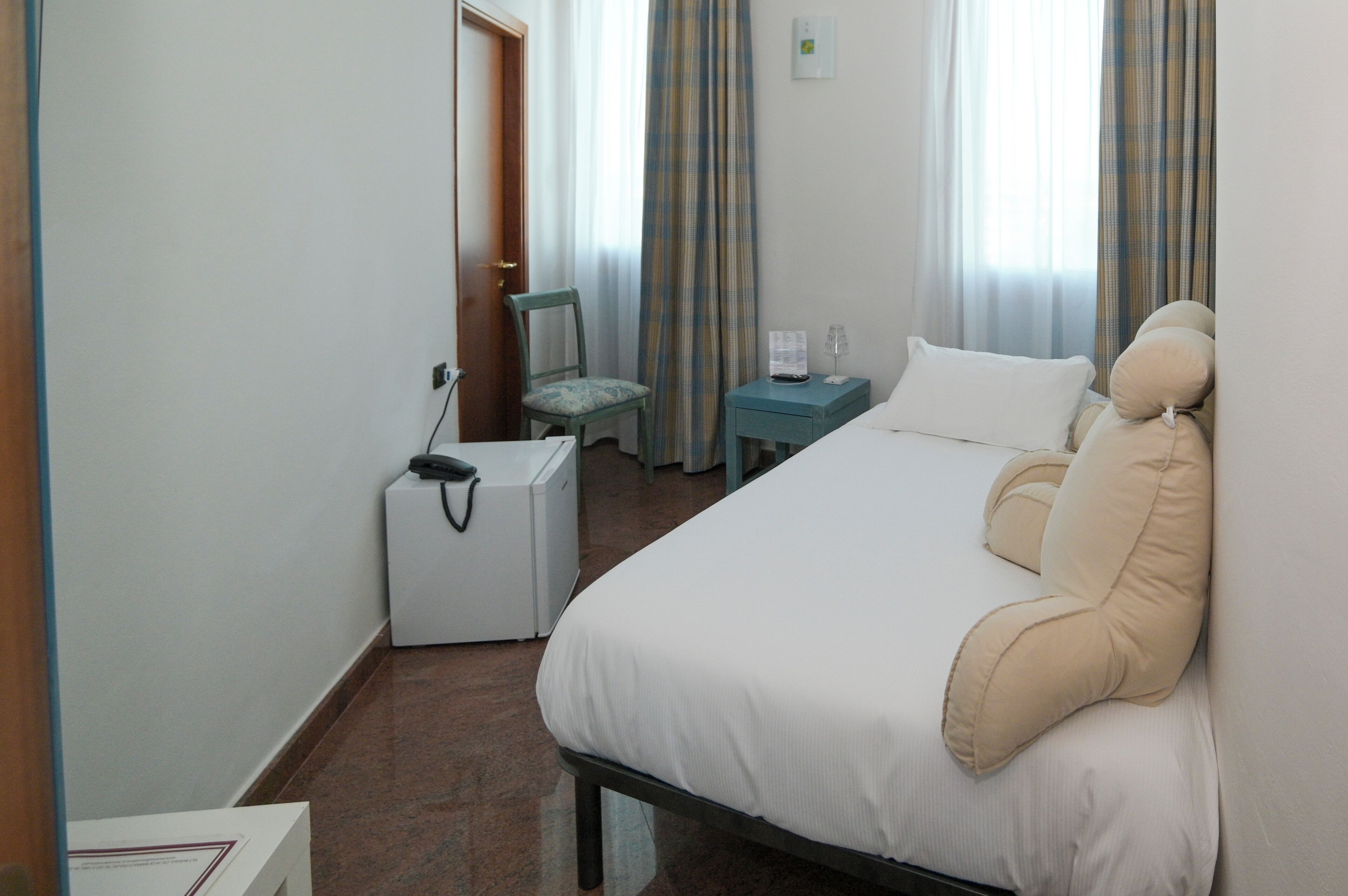 A hotel room with a bed, a chair, a small table with a lamp, and a suitcase.