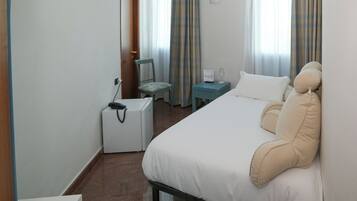 Ein Hotelzimmer mit Bett, Sessel, kleinem Tisch mit Lampe und Koffer.