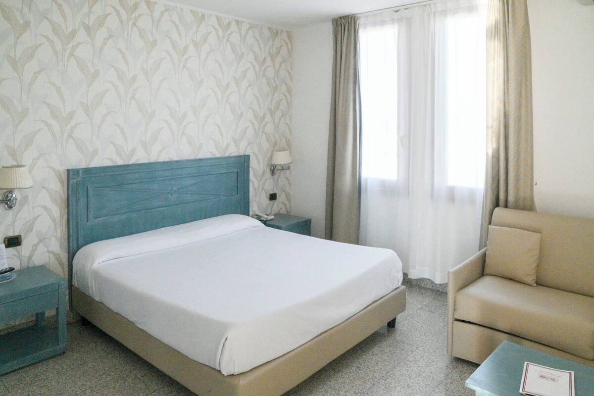 Una habitación de hotel con una cama, una mesita de noche, una lámpara, una silla y una pequeña mesa.