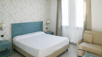 Une chambre d’hôtel avec un lit, une table de chevet, une lampe, une chaise et une petite table.