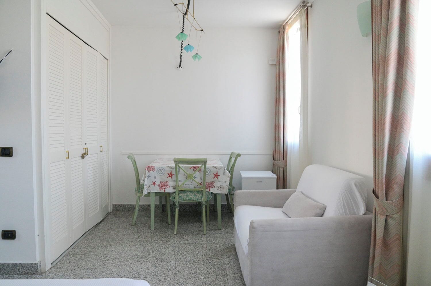 Una habitación pequeña y limpia con una mesa de comedor, dos sillas, un sofá, un armario y un adorno colgante.