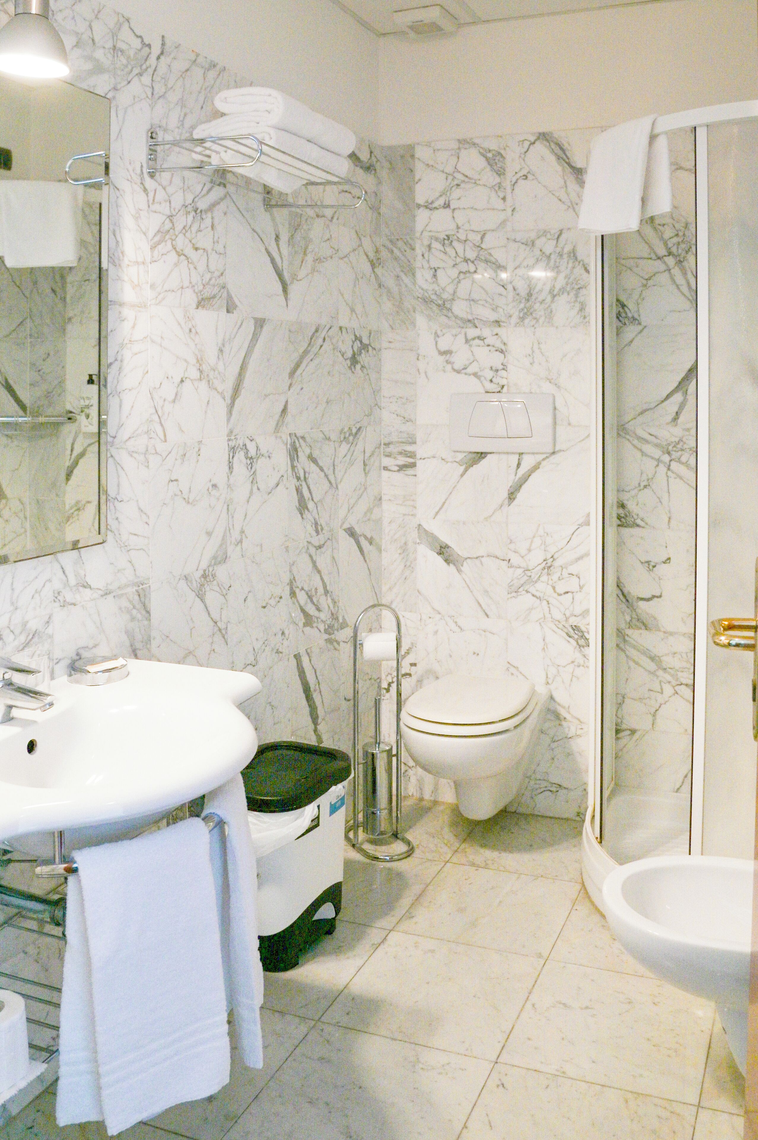 A bathroom with a marble wall, a sink, a toilet, and a shower.