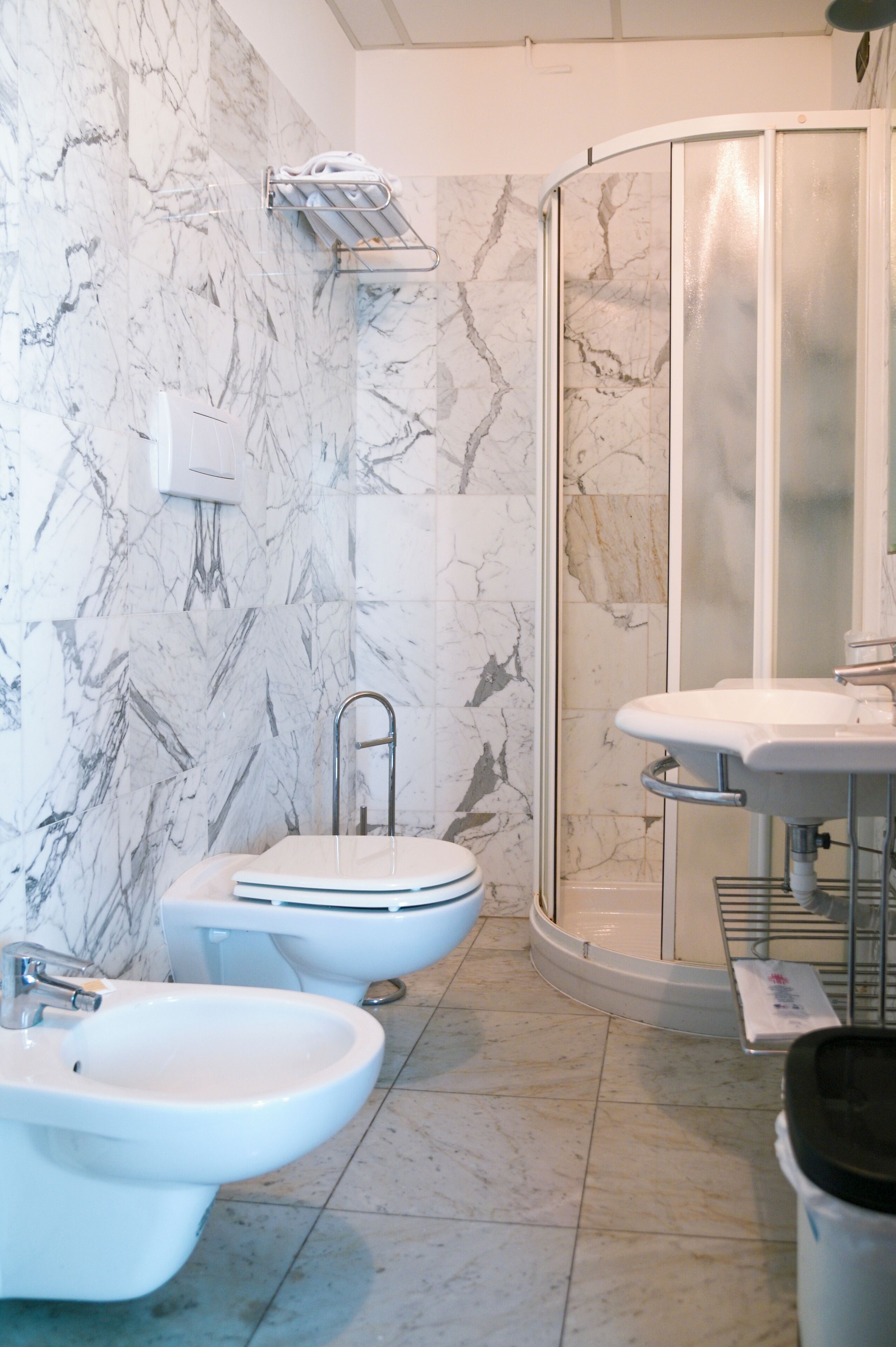 Un baño con pared de mármol, cabina de ducha, lavamanos y dos bidés.