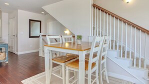 A dining area with a wooden table and white chairs, a staircase with white railings, and a small potted plant on the table. - Steps to Surf & Sand | Beachfront Oasis + Pier Walk (Pismo Beach)