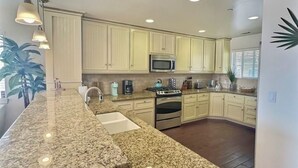 A kitchen with granite countertops, stainless steel appliances, and light-colored cabinetry. - Steps to Surf & Sand | Beachfront Oasis + Pier Walk (Pismo Beach)