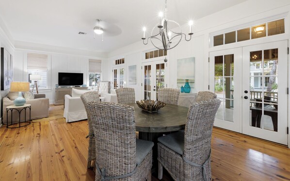 A spacious living room with a dining area, white walls, wooden flooring, and a large TV. - WaterColor Park District - Pools - Beach Access (Santa Rosa Beach)
