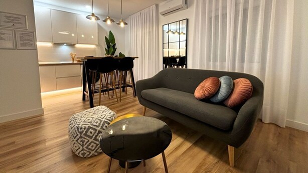 Una sala de estar moderna con sofá, reposapiés y zona de comedor.