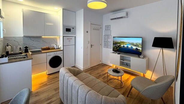 A modern living room with a sofa, chairs, a TV, and a kitchen area with appliances. - PIO XII XXI - B - Bright, central, and cozy apartment. - Deluxe 1 bedroom apartment (Talavera de la Reina)