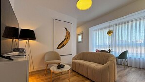 A modern living room with a sofa, a round coffee table, a lamp, and a framed banana artwork. - PIO XII XXI - B - Bright, central, and cozy apartment. - Deluxe 1 bedroom apartment (Talavera de la Reina)