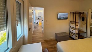 A bedroom with a bed, a desk, a chair, a TV, and a view of the city. - PIO XII XXI - B - Bright, central, and cozy apartment. - Deluxe 1 bedroom apartment (Talavera de la Reina)