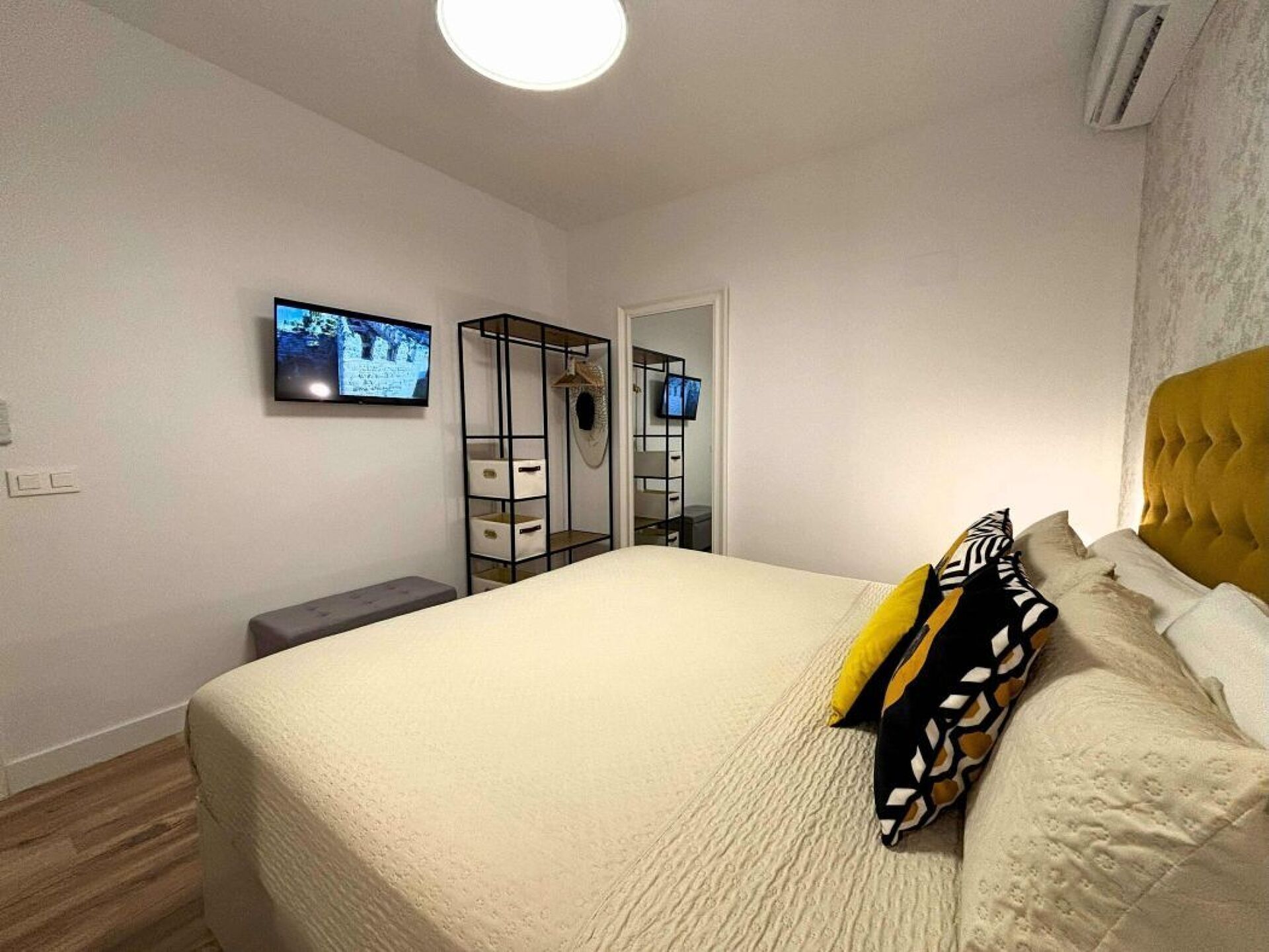 Een slaapkamer met een bed, een televisie, een kledingkast en een bankje.