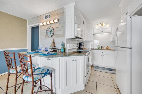 A kitchen with white cabinets, a central island with chairs, a clock, and a coffee maker.