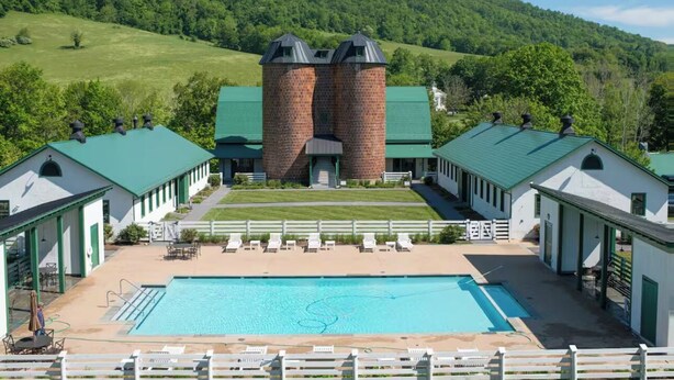 A pool area with a large rectangular pool, surrounded by lounge chairs and a brick building with two towers in the background. - Across from the Springs, Access to Pool + Hot Tub (Warm Springs)