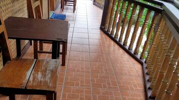 A covered outdoor area with tiled flooring, wooden furniture, and a railing overlooking greenery.