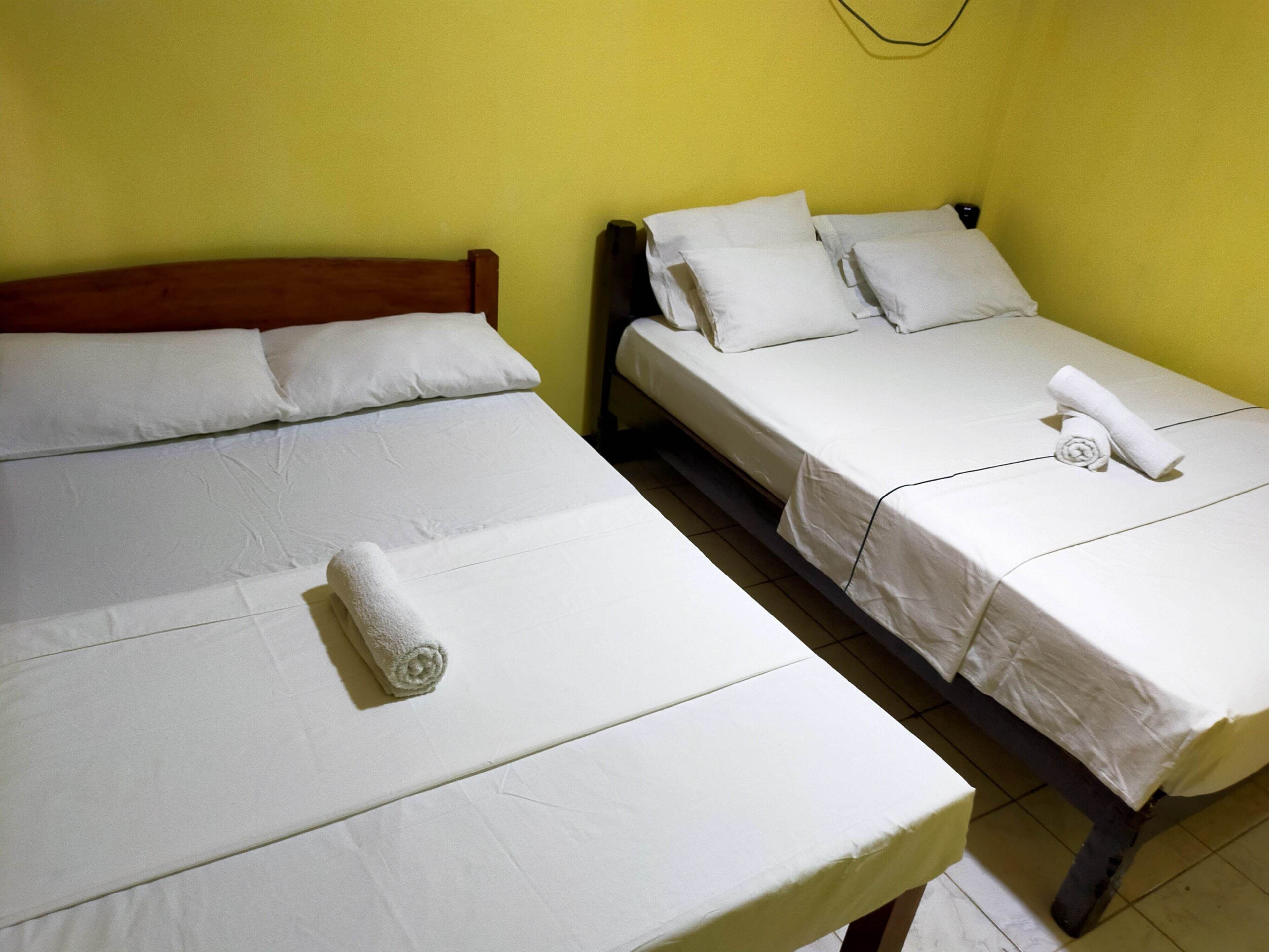 Dos camas individuales con sábanas y almohadas blancas, un cabecero de madera y una pared amarilla.