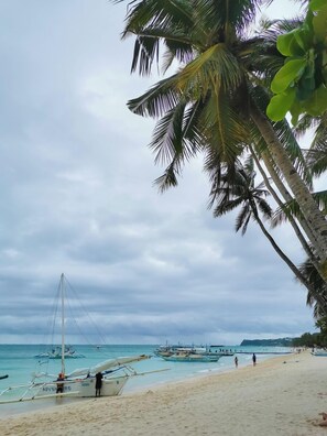 Ein Strand mit Booten, Palmen und einem bewölkten Himmel.