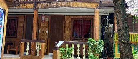 A traditional wooden building with a balcony, stone flooring, and potted plants.