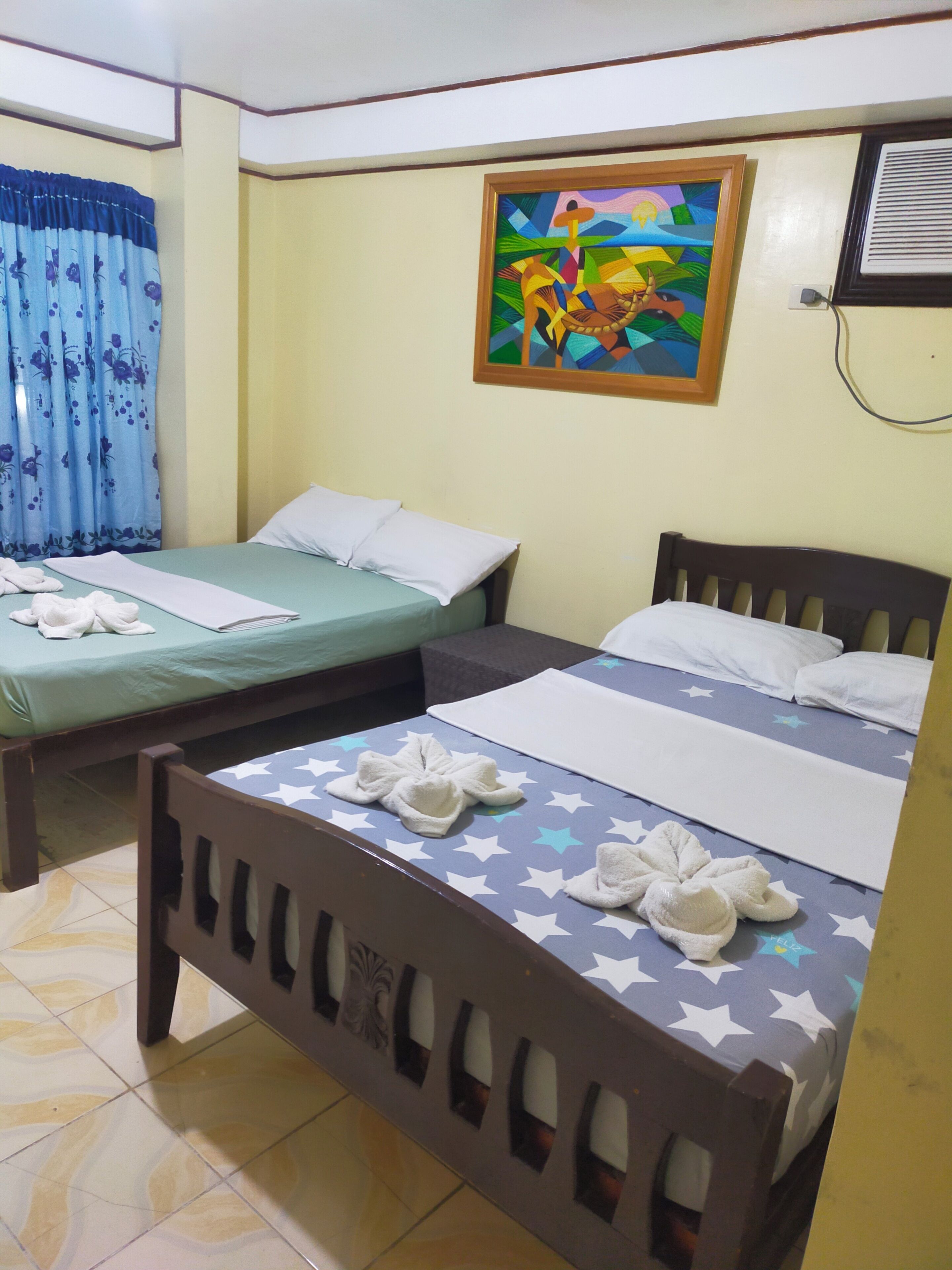A hotel room with two beds, a painting on the wall, and a window with curtains.