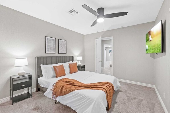 A bedroom with a bed, nightstands, a ceiling fan, and framed artwork on the wall.
