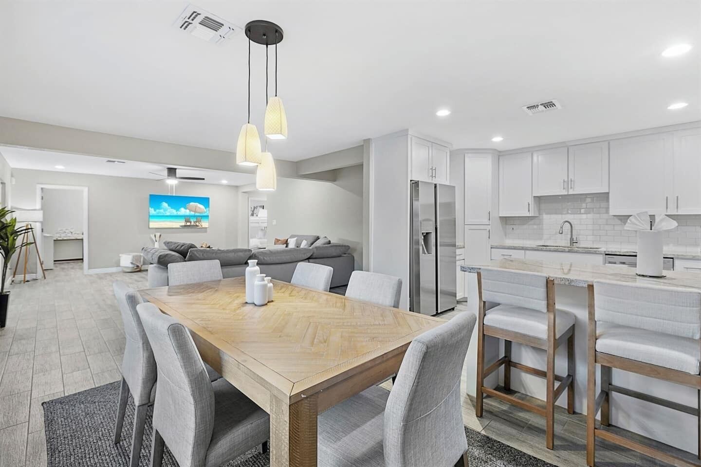 A modern kitchen with white cabinets, a stainless steel refrigerator, and a bar area with stools.