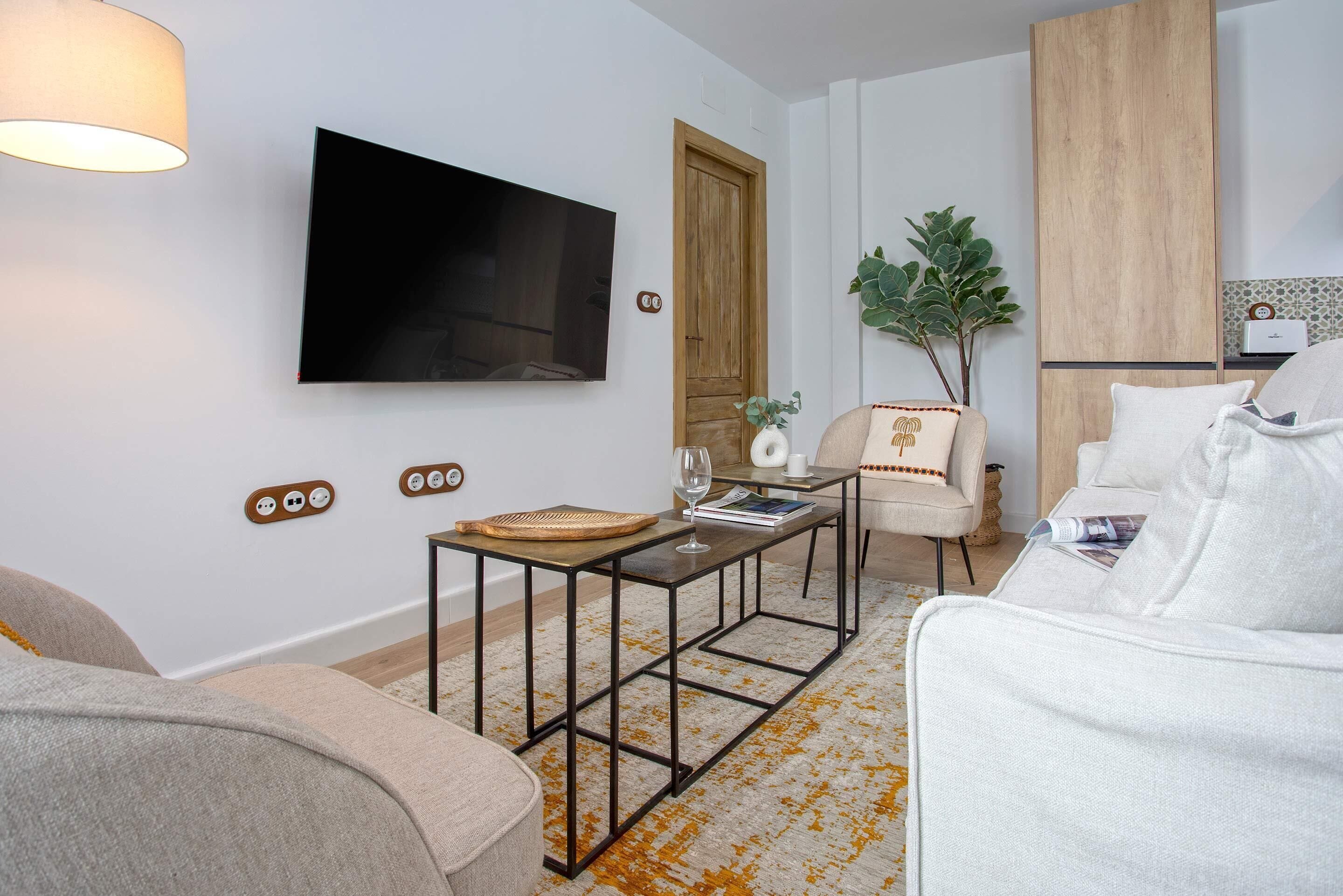 A modern living room with a flat-screen TV, a coffee table, a sofa, and a small side table with a plant.