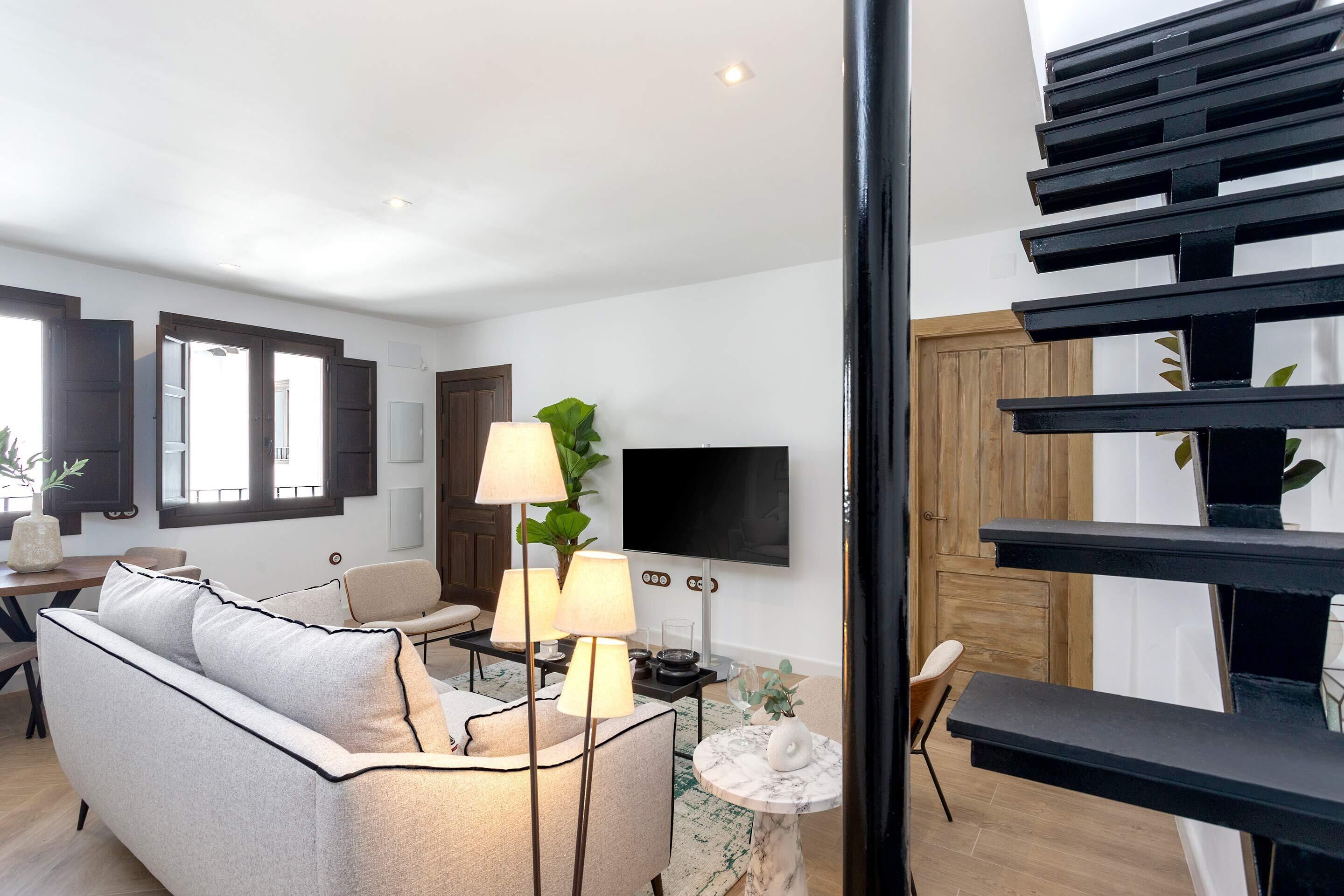 A modern living room with a sofa, lamps, a TV, and a staircase.